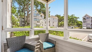 Un espace extérieur aménagé, abrité et doté de chaises en osier, offrant une vue sur des immeubles à plusieurs étages.