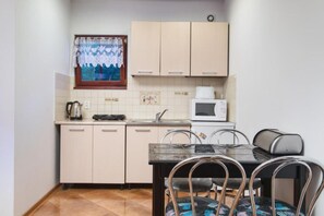 A compact kitchen with a dining table, chairs, a microwave, and a window with a curtain. - Scandinavian Cottage With Private Garden (Choczewo)
