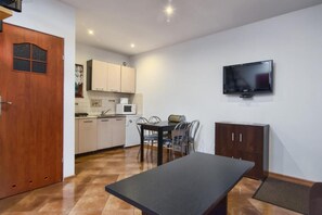 A compact kitchen with a dining area, a TV mounted on the wall, and a wooden door. - Scandinavian Cottage With Private Garden (Choczewo)