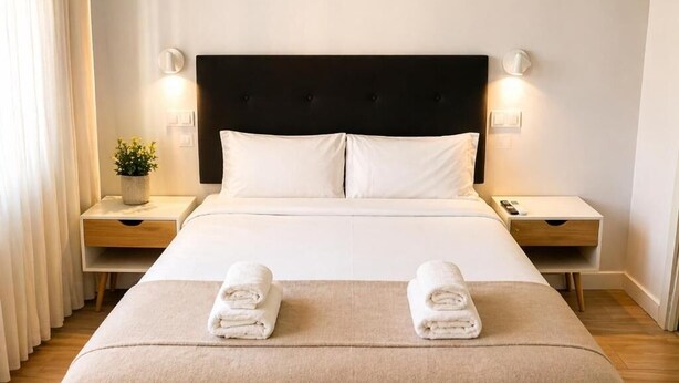 Habitació d'hotel amb un llit, dues taules de nit, una taupinyot, una làmpada i una planta.