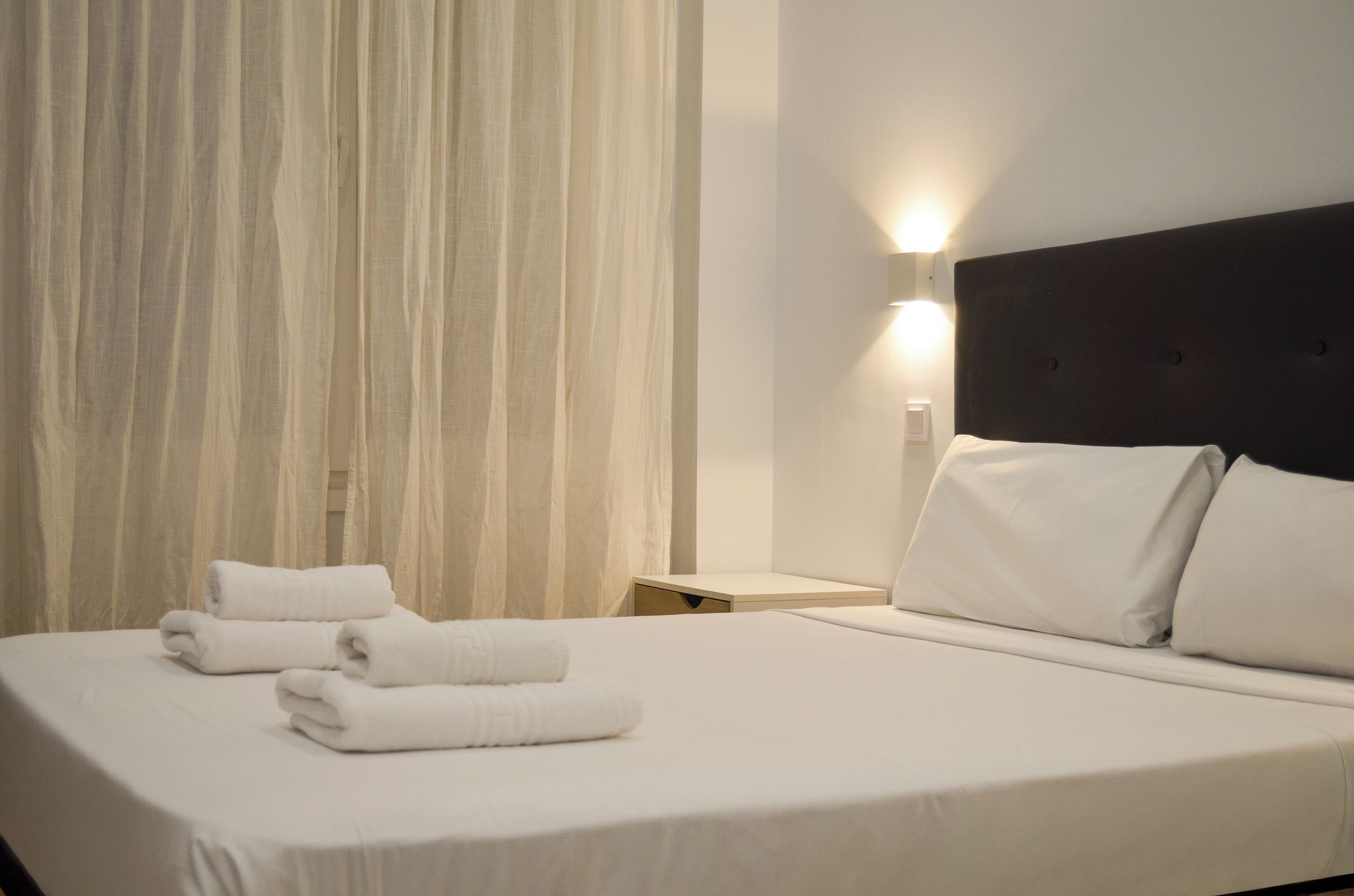 A hotel room with a bed, a nightstand, and a wall-mounted light.