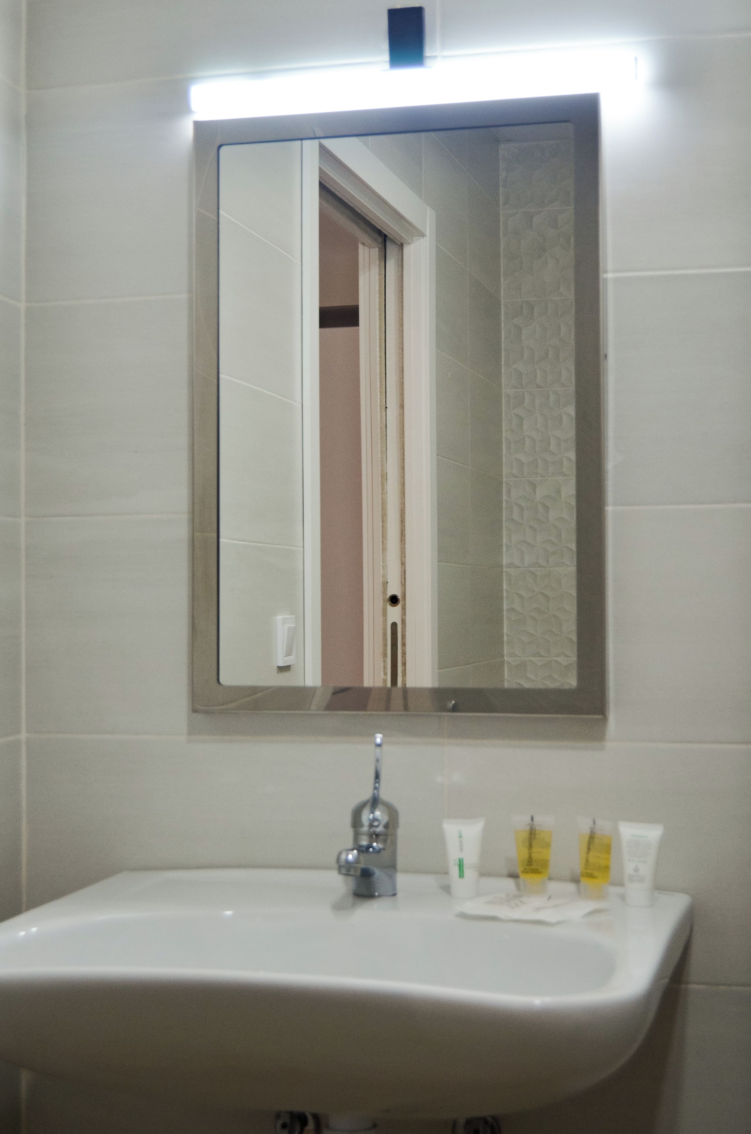 A bathroom with a white sink, a mirror, and toiletries on the counter.