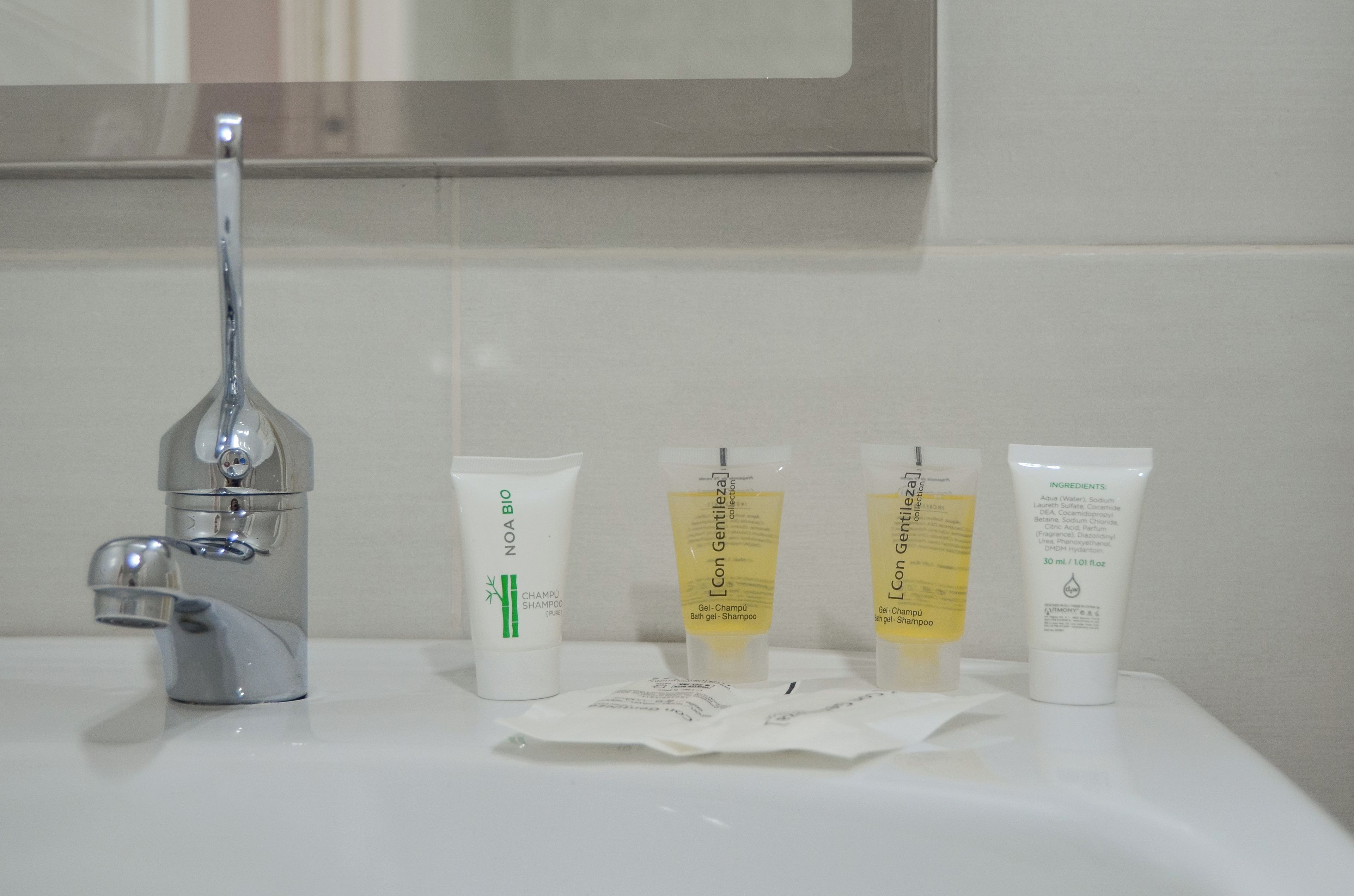 A bathroom sink with three toiletries: a shampoo bottle, a bath gel, and a shampoo bar.