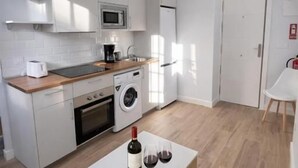 Una cuina moderna amb armaris blancs, microones, rentadora i zona de menjador amb taula i caires.