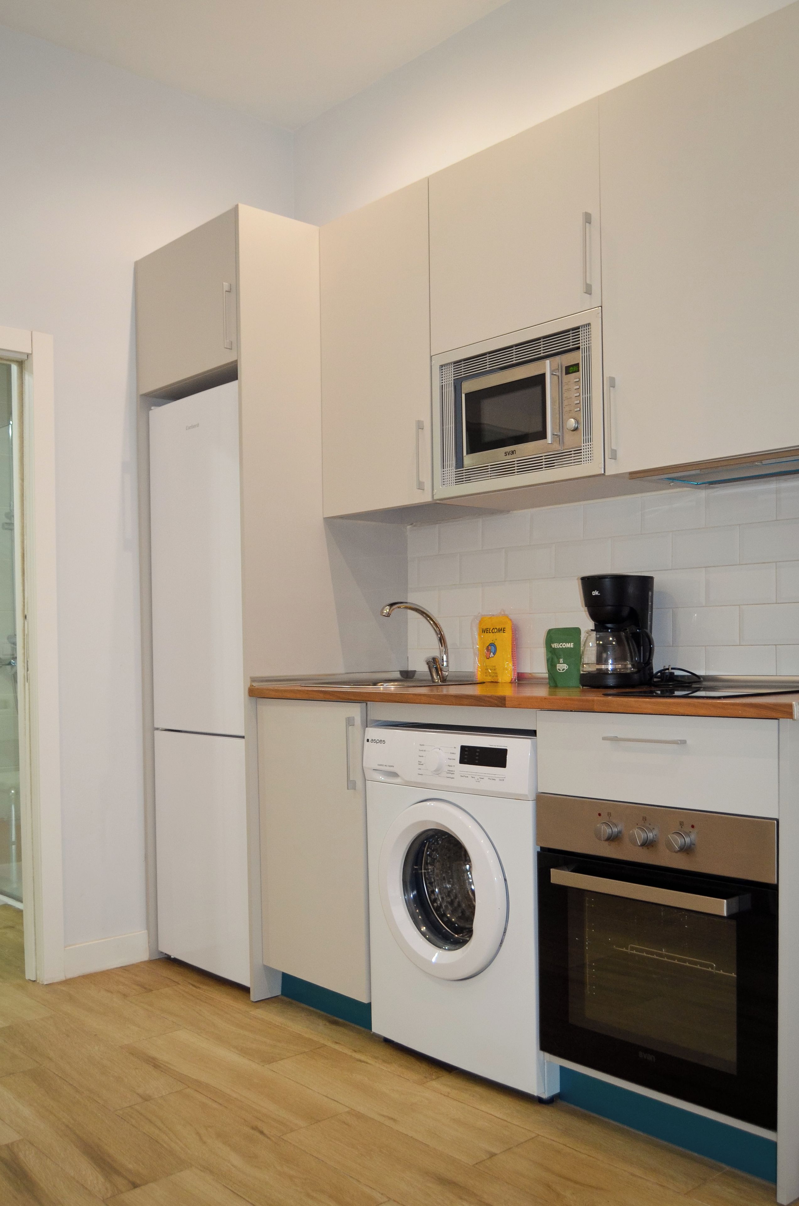 A compact kitchen with a washing machine, a microwave, and a coffee maker.