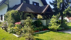 A house with a sloped roof, a garden with various plants and flowers, and a wooden bench. - Large and Comfortable Holiday Villa With a Garden (Choczewo)