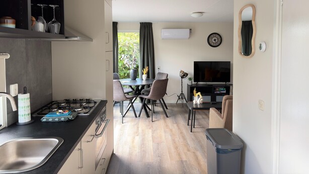 A modern kitchen with a dining area, a TV, and a large window with curtains. - Chalet 56 in Stegeren Near the Heathlands (Stegeren)