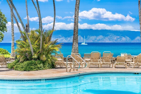A pool with lounge chairs and palm trees, overlooking a clear blue ocean and distant mountains. - New Listing! Cozy studio for 4 in steps from the beach - Napili Shores C120 (Lahaina)