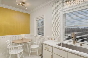A kitchen with white cabinetry, a wooden table with chairs, a window with blinds, and a view outside. - *NEW* Cozy Chic 1BR Downtown Chattanooga (Chattanooga)