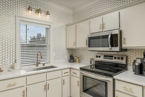 A kitchen with white cabinets, a stainless steel oven, a microwave, and a window with blinds. - *NEW* Cozy Chic 1BR Downtown Chattanooga (Chattanooga)