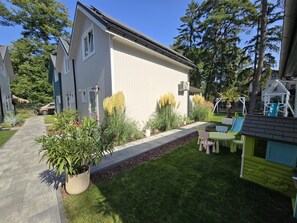 A residential property with a paved driveway, a lawn, a play area with a slide, and a large window on the house. - Large Holiday Homes With Beautiful Gardens (Rewal)