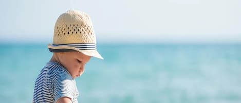 A child playing with toys on a sandy beach with the ocean in the background.