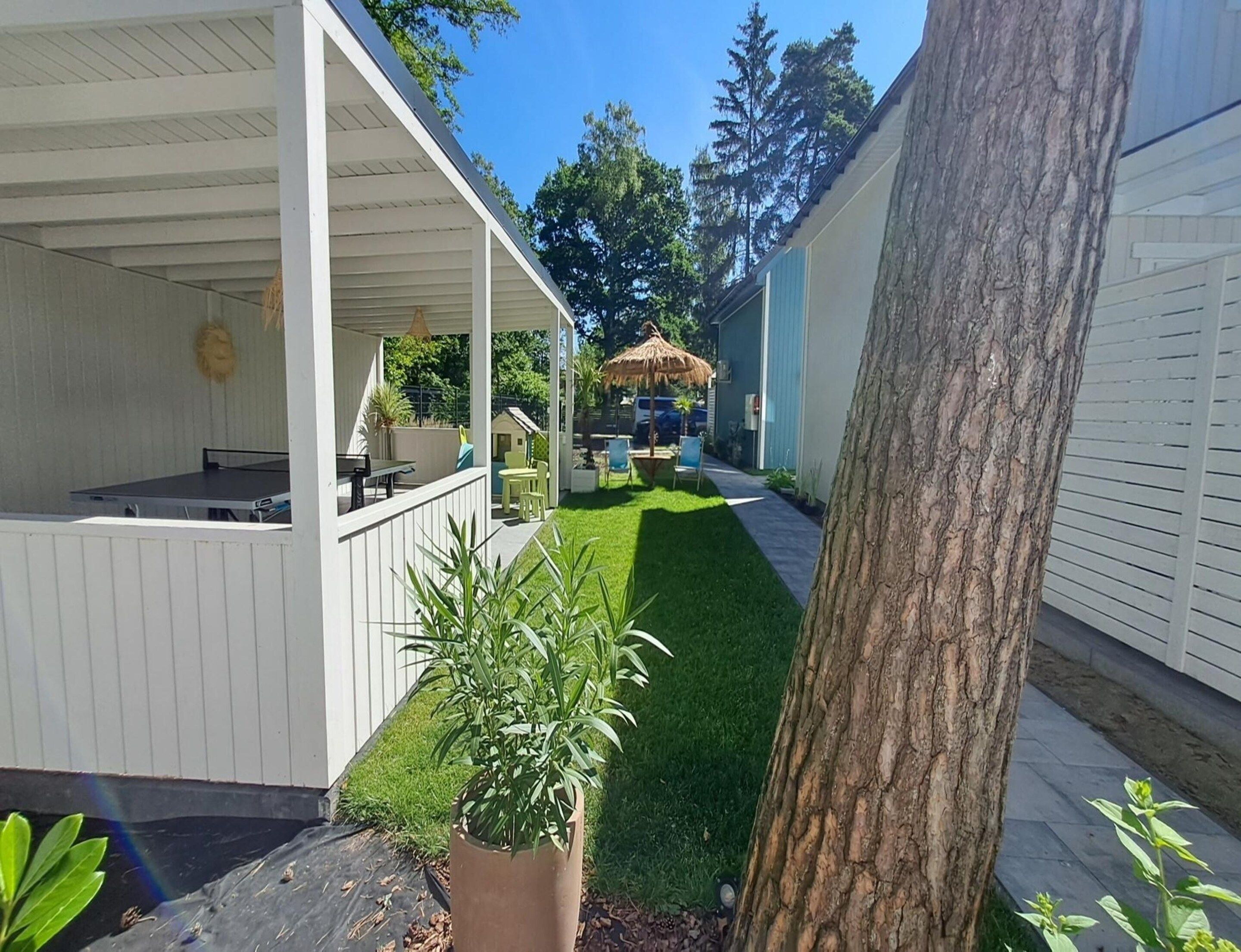 Ein überdachter Außenbereich mit Tisch und Stühlen, ein kleiner Garten mit Baum und ein Gebäude mit Strohdach.