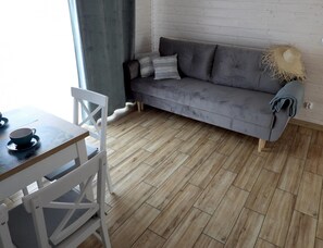 Ein Zimmer mit einer grauen Couch, einem Holzesstisch und weißen Stühlen.