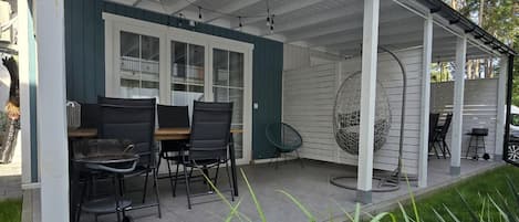 A covered patio with a table and chairs, a hanging chair, and a grill area.