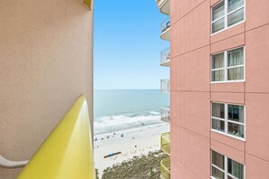 Ein Balkon mit Blick auf den Strand und den Ozean, ein rosafarbenes Gebäude und ein gelbes Geländer.