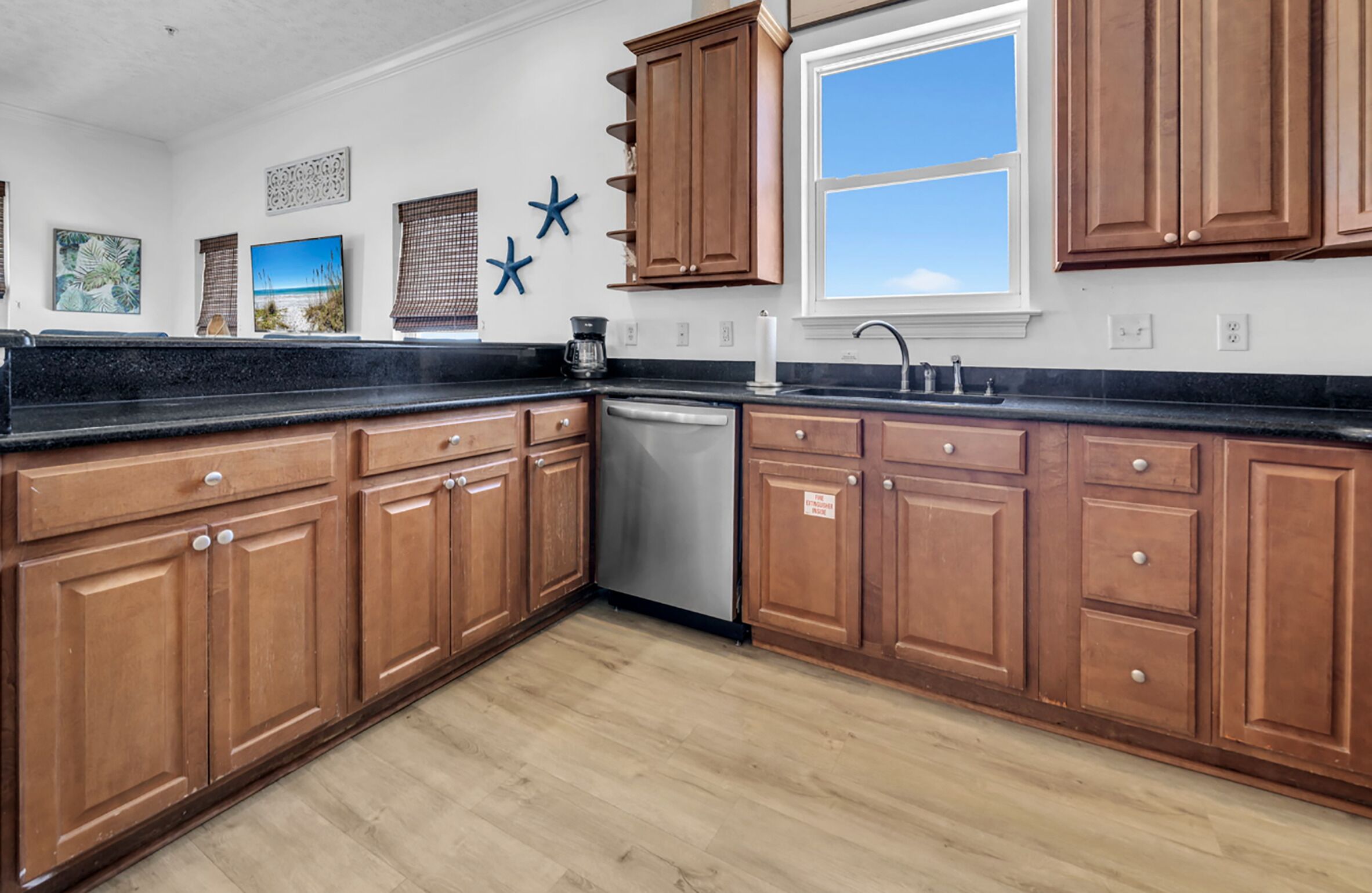 A kitchen with wooden cabinets, a dishwasher, and a window with blinds.