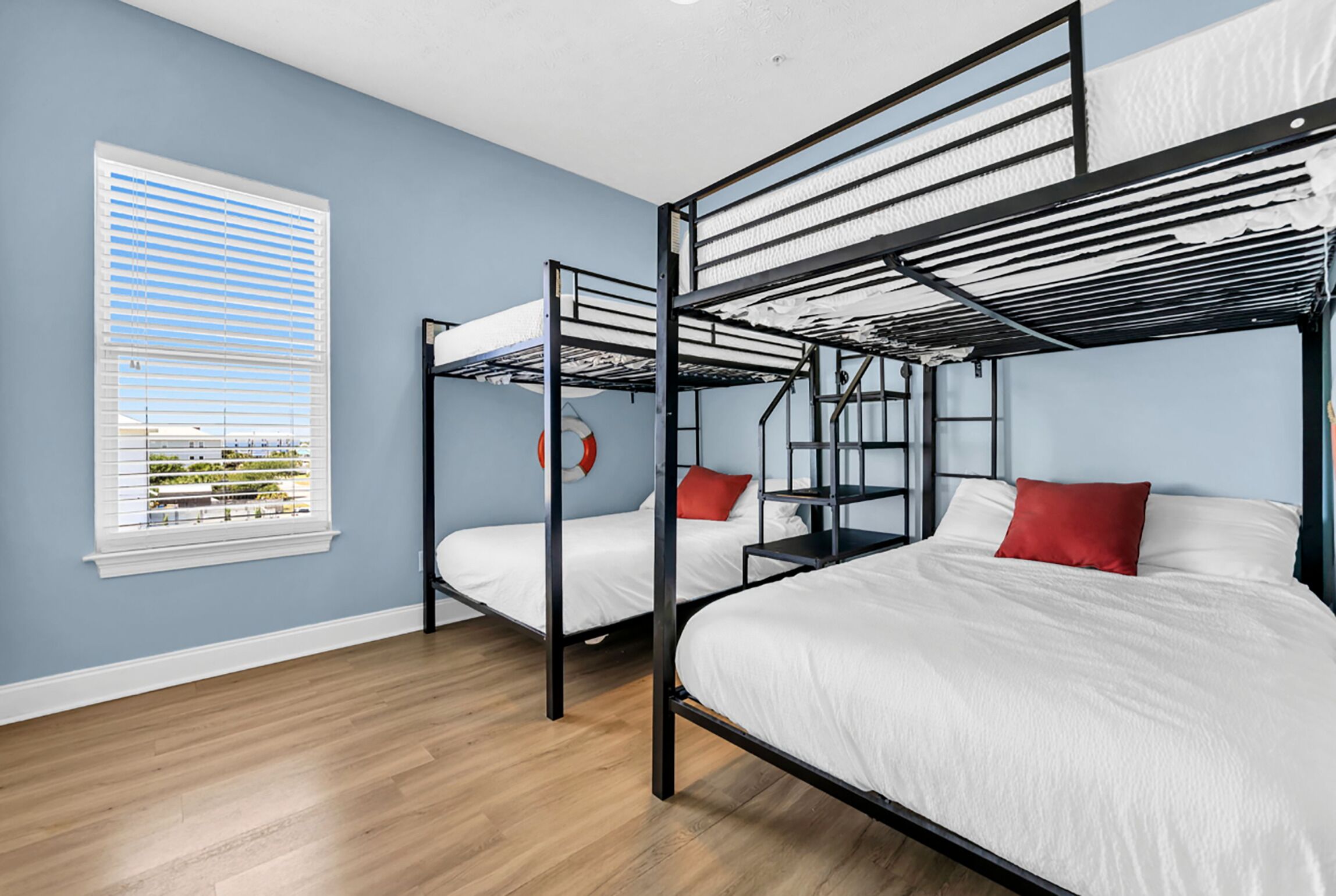 A room with bunk beds, a window with blinds, and a view of greenery outside.