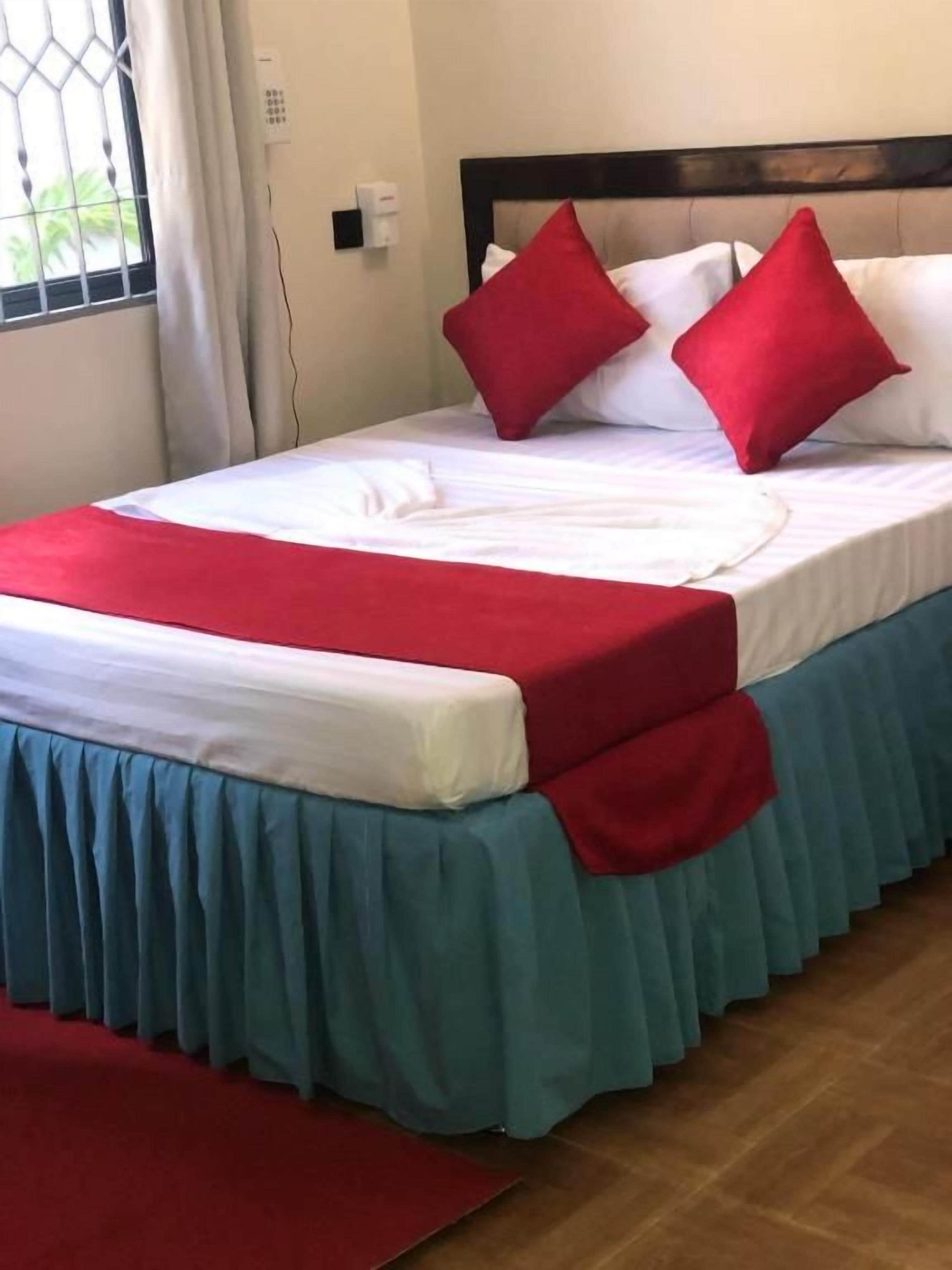 A bed with a white mattress, red and blue bed skirt, and two red pillows.