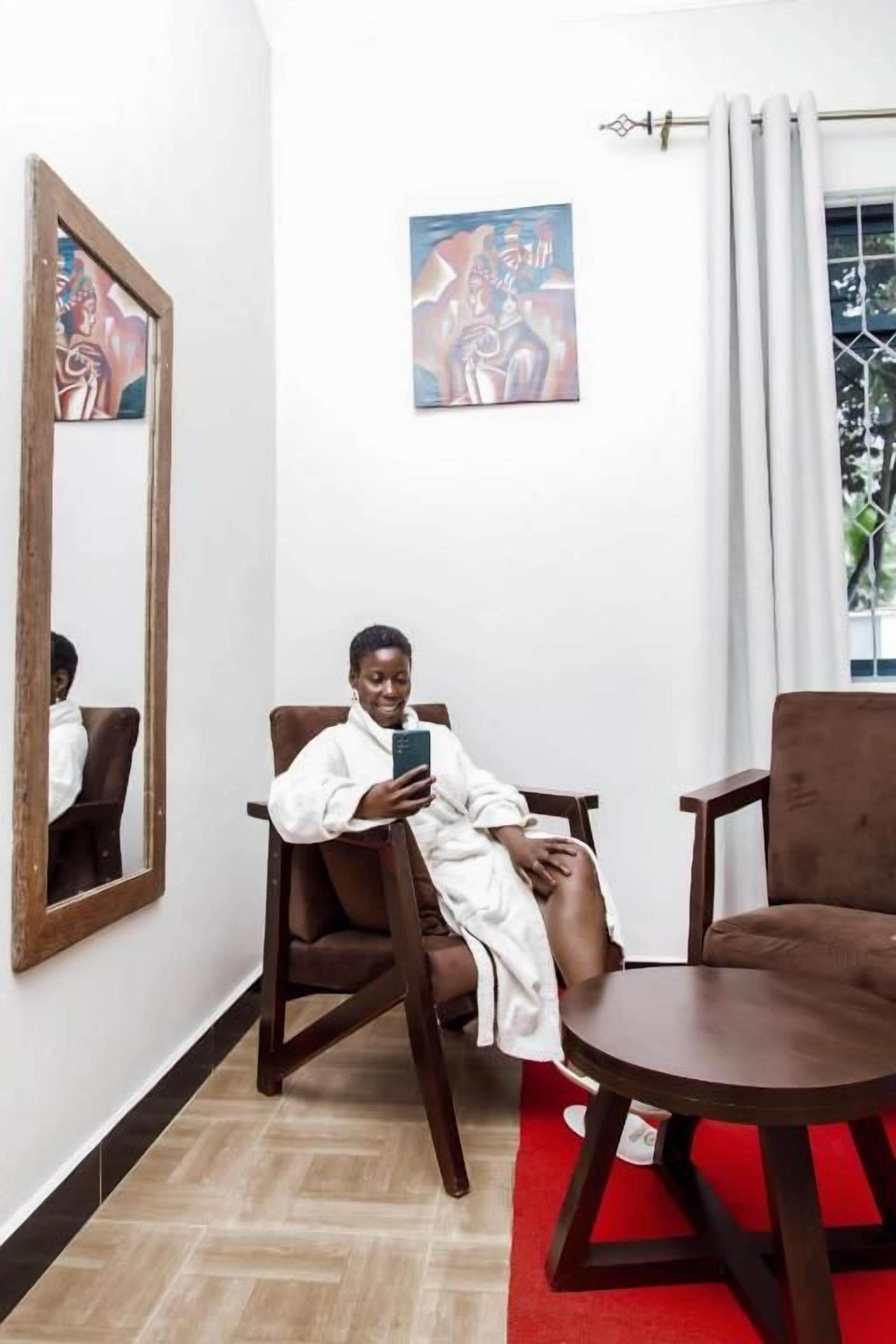 A room with a large mirror, a painting on the wall, and a person sitting on a chair.