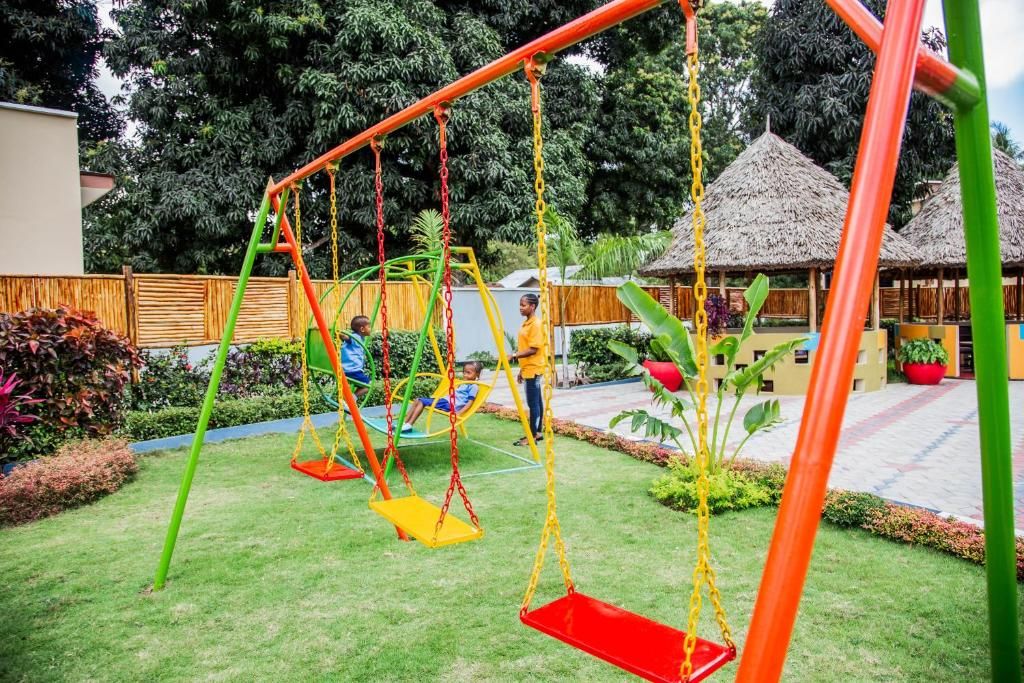 Un parque infantil con columpios y una estructura de techo de paja al fondo.