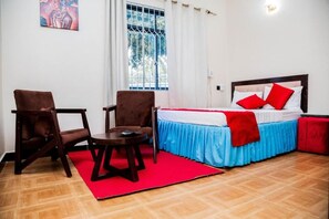 A hotel room with a bed, two armchairs, a small table, and a window with curtains. - Family Ties Inn (Bagamoyo)