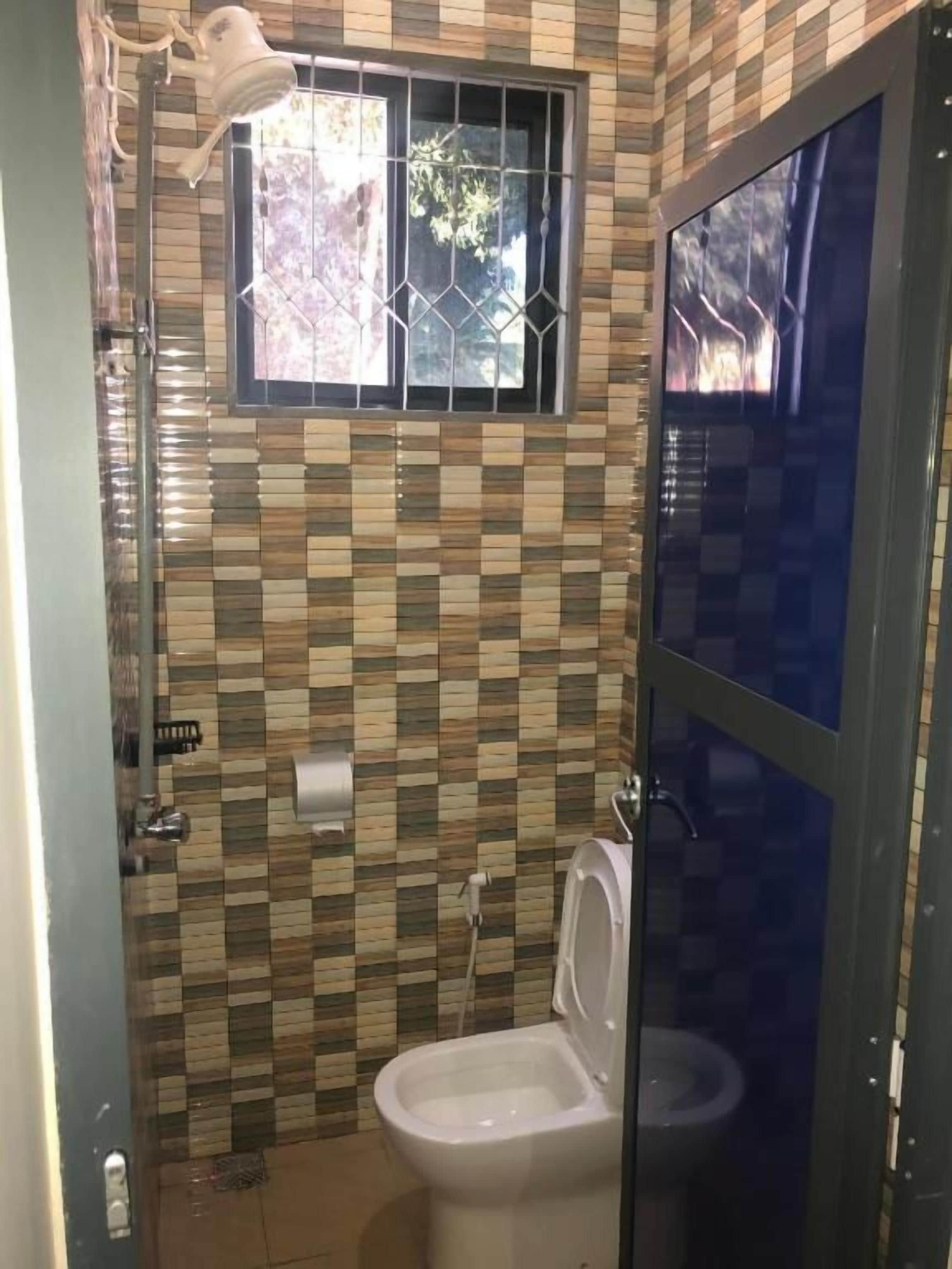 A bathroom with a tiled wall, a toilet, a sink, and a window with a metal grille.
