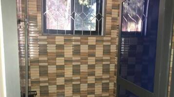 A bathroom with a tiled wall, a toilet, a sink, and a window with a metal grille.