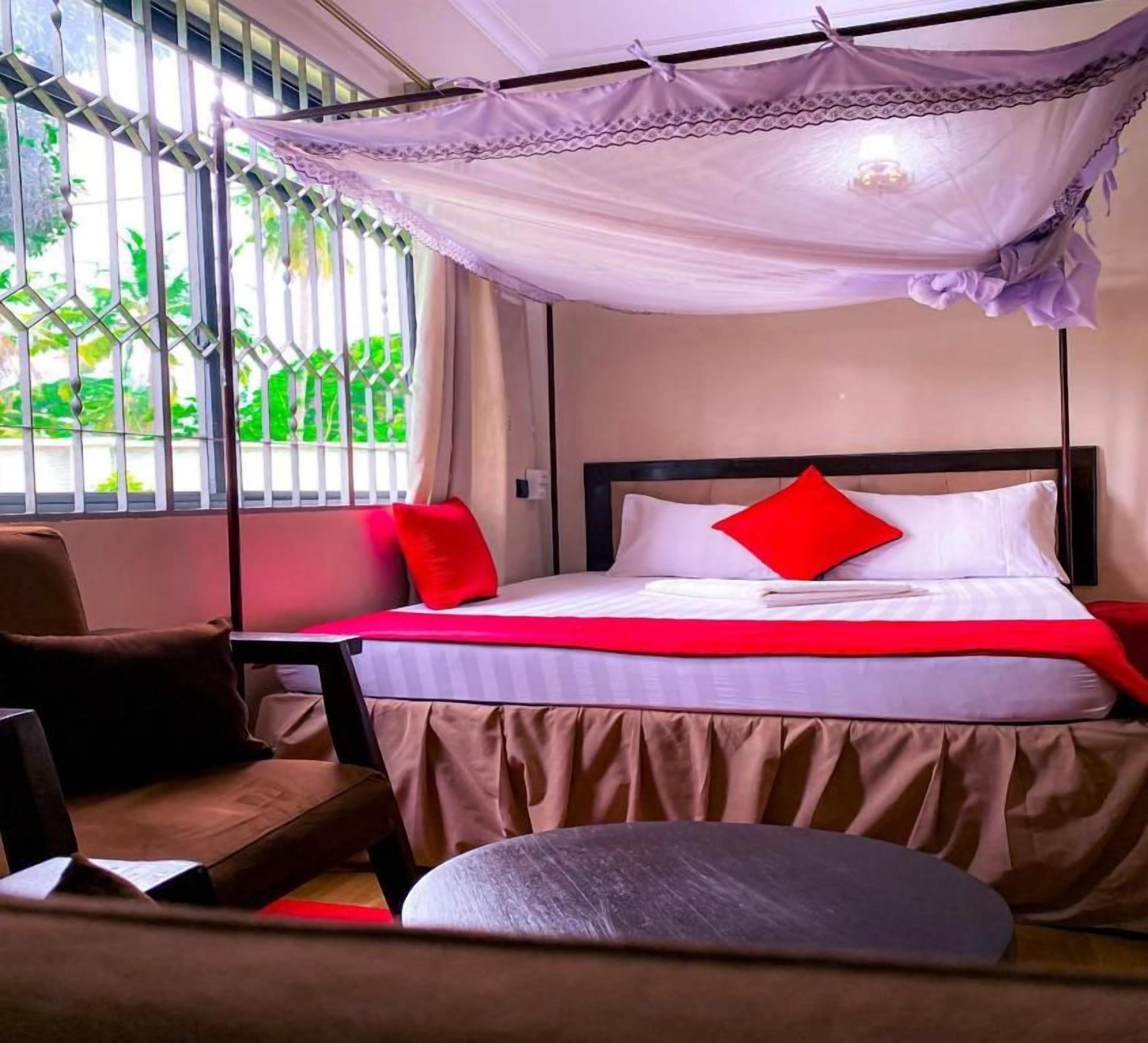 A bed with a canopy, a chair, and a view of greenery outside.