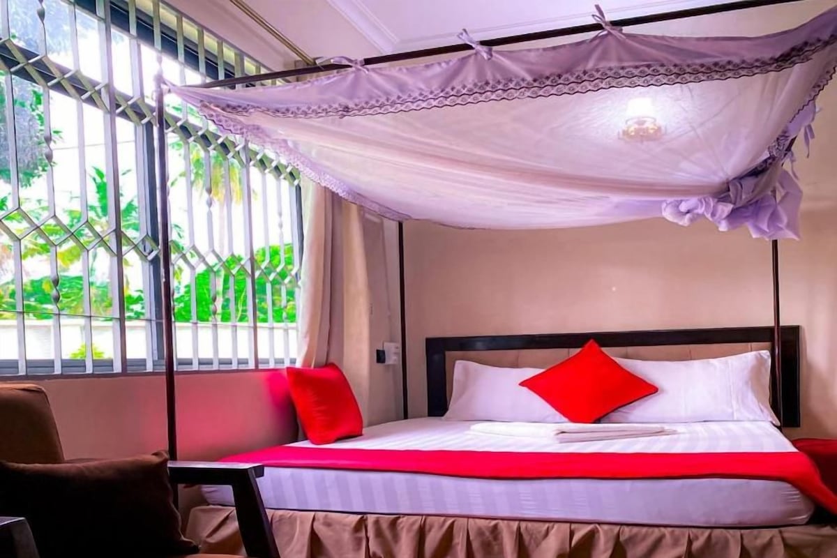 A bed with a canopy, a chair, and a view of greenery outside.