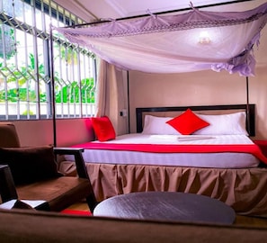 A bed with a canopy, a chair, and a view of greenery outside. - Family Ties Inn (Bagamoyo)
