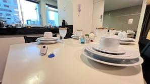 Comedor de hotel con una mesa preparada para cuatro personas, incluyendo platos, vasos y un control remoto.