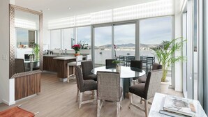 Een moderne keuken met een groot eiland, een eethoek met een ronde tafel en stoelen, en grote ramen met uitzicht op de stad.