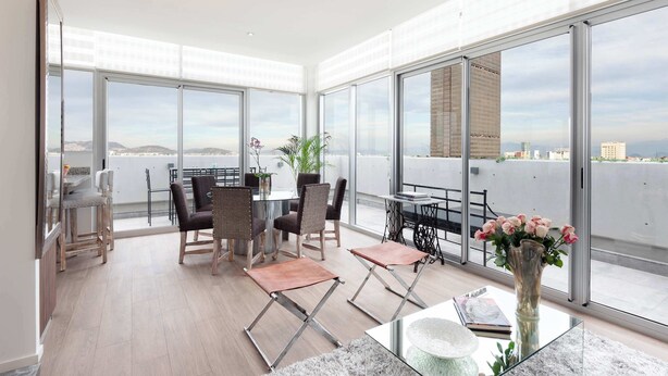 Een ruim balkon met een eethoek, grote ramen en uitzicht op de stad.