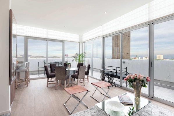 Ein geräumiger Balkon mit Essbereich, großen Fenstern und Blick auf die Stadt.