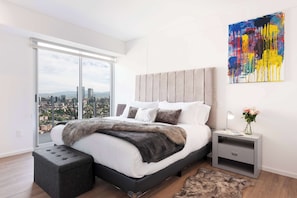 Ein modernes Schlafzimmer mit einem großen Bett, einem Nachttisch, Blick auf die Stadt und einem farbenfrohen, abstrakten Gemälde.