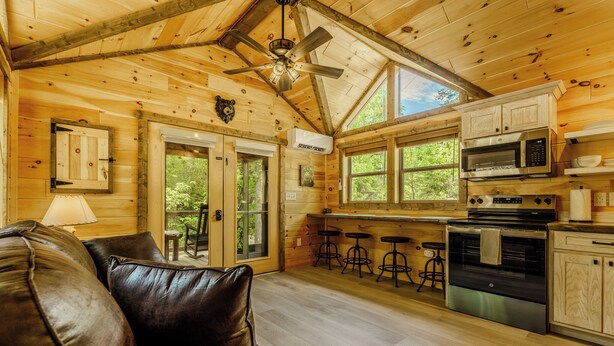 Interior de una cabaña de madera con cocina, comedor y un sofá de cuero.