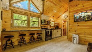 Interior de una cabaña de madera con cocina, taburetes de bar, un reloj y un cartel que dice 'Serenity... Smokies'.