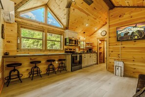 En stuga med träpanel på insidan, inredd med ett kök, barstolar, en klocka och en skylt med texten ”Serenity... Smokies”.