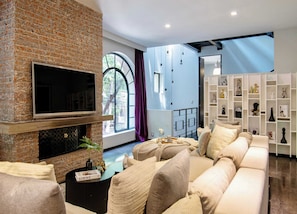 Ein Wohnzimmer mit Kamin aus Ziegelsteinen, einem großen Fernseher, einer Couch und einem Bücherregal mit Dekoration.