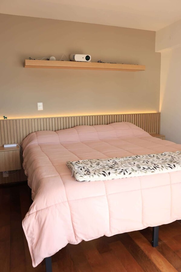A bedroom with a bed, a bedside table, a wall-mounted shelf, and a radiator.