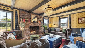 A cozy living room with a fireplace, leather sofas, a chandelier, and a large window. - Cedar Hall - A Charming Vintage Estate (Lebanon)