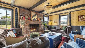 A cozy living room with a fireplace, leather sofas, a chandelier, and a large window.