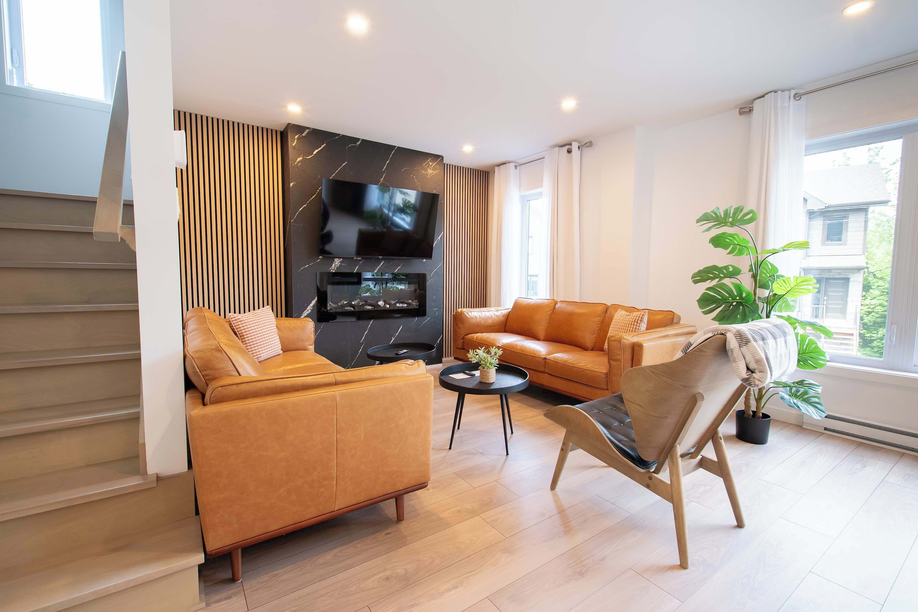Un salon moderne avec un canapé, un fauteuil, un téléviseur, une cheminée et une grande fenêtre.
