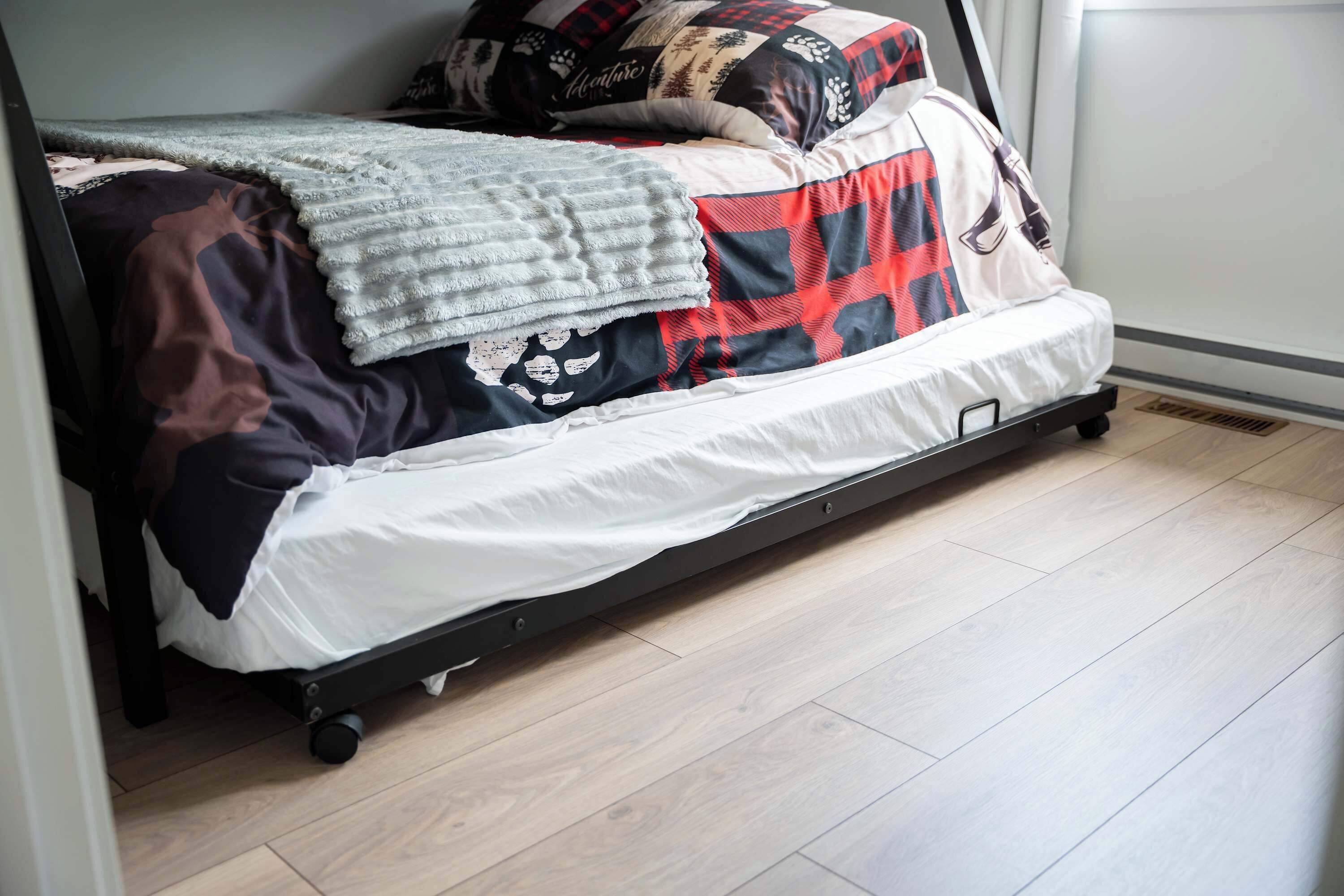 A bed with a black metal frame, a white mattress, and a red and black plaid blanket.
