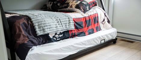 A bed with a black metal frame, a white mattress, and a red and black plaid blanket.