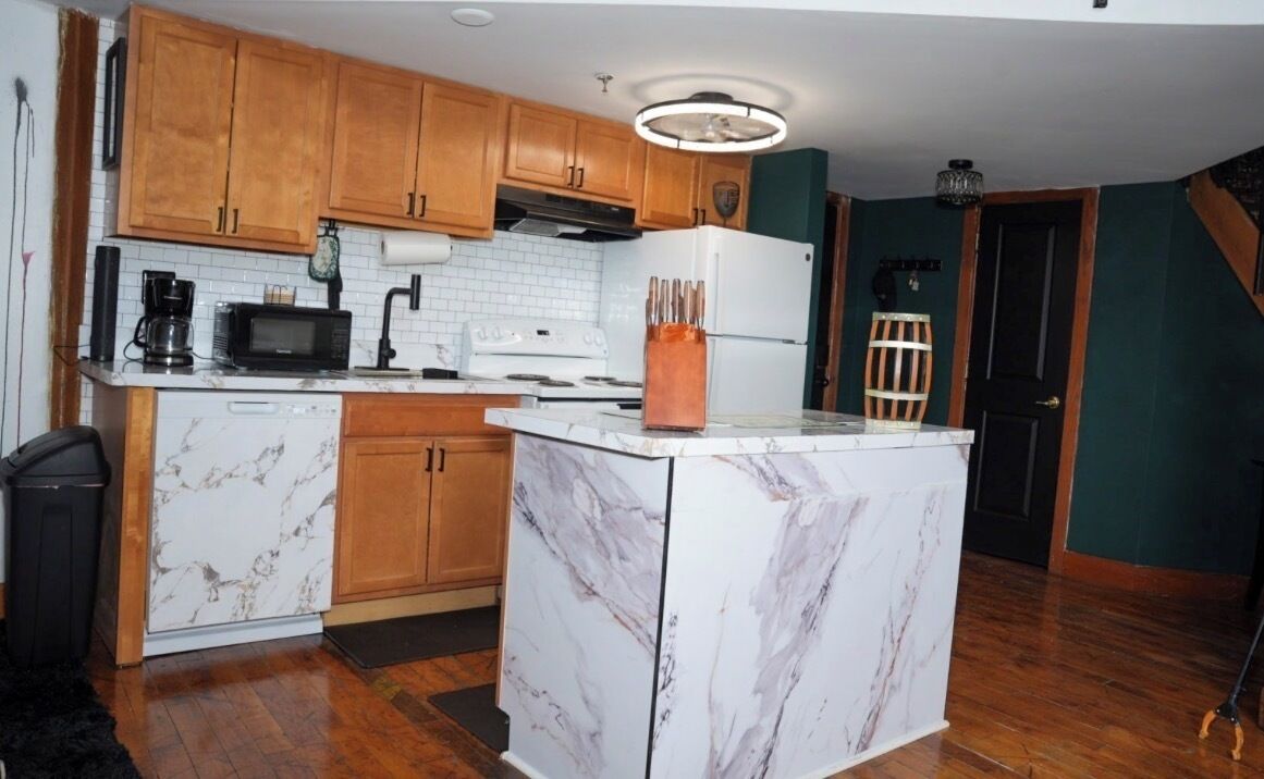 A kitchen with wooden cabinets, a white marble island, a microwave, a stove, and a refrigerator.