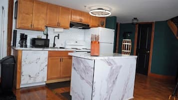 A kitchen with wooden cabinets, a white marble island, a microwave, a stove, and a refrigerator.
