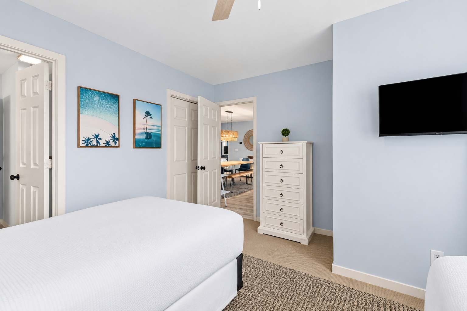Une chambre à coucher avec un lit, une commode, un téléviseur et deux tableaux accrochés au mur.