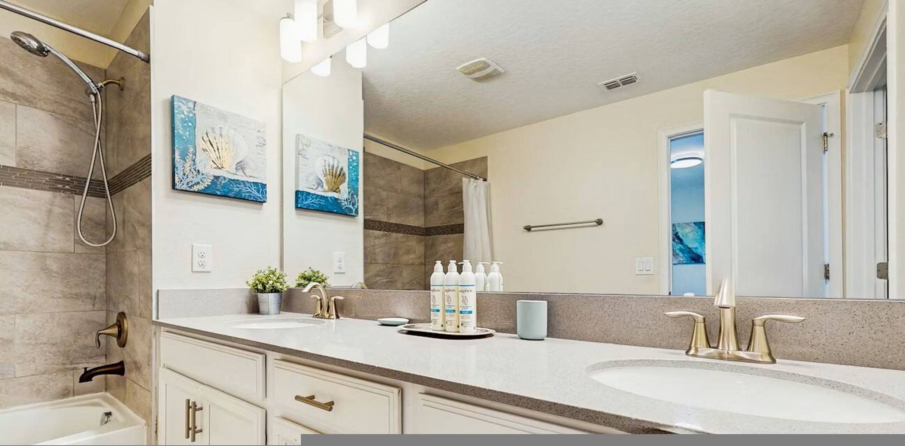 A bathroom with two sinks, a shower, and a large mirror. There are decorative wall art pieces and a towel rack.